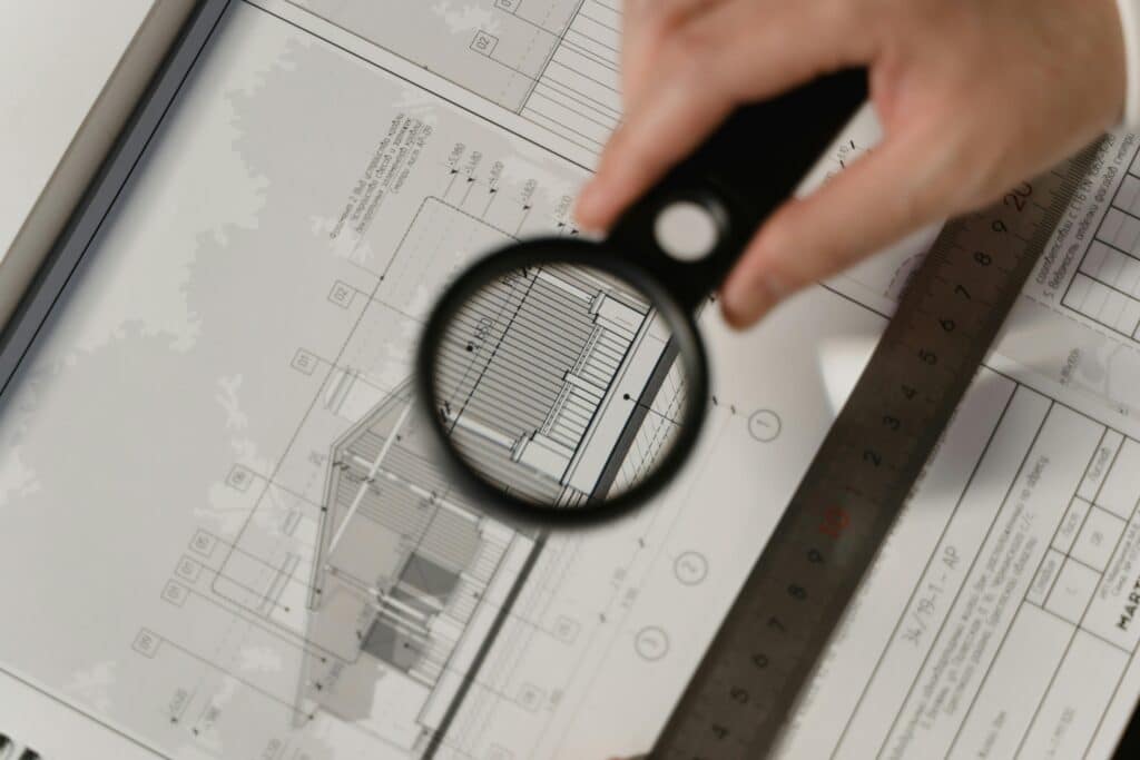 Plan architecture : vérification précise des détails à la loupe. Focused view of architectural plans with magnifying glass, ruler, hands.